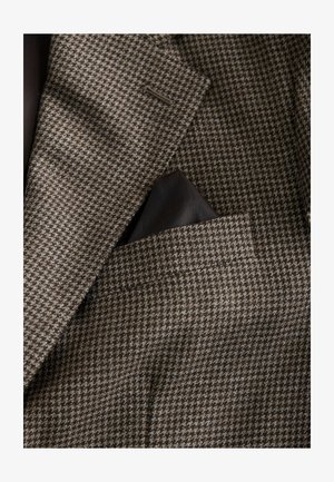 Blazer dengan pola houndstooth coklat yang terbuat dari kain tekstur. Termasuk pocket square yang terselip di saku dada. Lining bagian dalam terlihat.