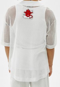 Valkoinen verkkopaita ylisuurilla mitoilla, jossa punainen piirretty paholainen pilven päällä takana. Pyöristetty helma ja lyhyet hihat.