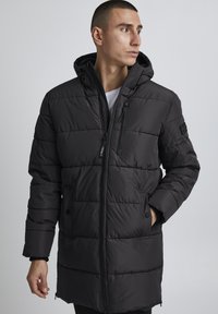 Black puffer jacket with a hood, featuring quilted texture, zippered front, side pockets, and a modern cut. Accents in matte fabric.