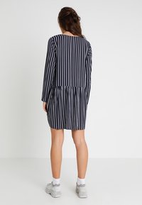 Sukienka w niebiesko-białe paski z długimi rękawami, okrągłym dekoltem i marszczoną talią, charakteryzująca się luźnym krojem i miękką fakturą materiału.