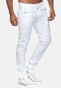 Weiße Baumwollhosen mit geradem Schnitt, vorderen Taschen und kontrastierenden Nähten. Kombiniert mit weißen Turnschuhen, die einen lässigen Stil zeigen.