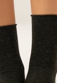 Black ankle socks made of textured fabric with a slight sheen and fuzzy appearance, featuring a ribbed cuff.