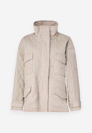 Veste beige matelassée avec un col montant, quatre poches à l'avant et un contraste de tissu texturé. Des plis aux poignets ajoutent une touche de détail.
