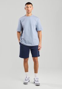 Light blue cotton t-shirt with short sleeves, paired with navy shorts. White sneakers with gray accents. Simple, relaxed fit.