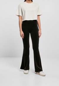 Przycięta jasnobeżowa koszulka z krótkim rękawem w połączeniu z czarnymi spódniczkami w stylu dzwonów z miękkiego materiału; dopełniona białymi trampkami.