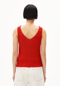 Rood geribbeld gebreid tanktop met een V-hals achterkant, mouwloos ontwerp en een aangesloten silhouet, gecombineerd met crèmekleurige hoge taille jeans.