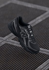 Chaussure de sport noire avec dessus en maille, accents réfléchissants, col rembourré et design à lacets. Comprend une semelle rembourrée pour un soutien optimal.