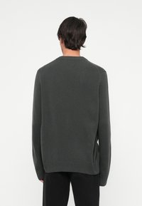 Ciemnozielony dzianinowy sweter z długimi rękawami, ściągaczami przy mankietach i u dołu. Prosty krój z okrągłym dekoltem i luźnym fasonem.