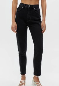 Jean en denim noir taille haute avec une taille ajustée, des jambes droites, cinq poches et des détails argentés sur les boutons et rivets. L'ourlet est légèrement effiloché.