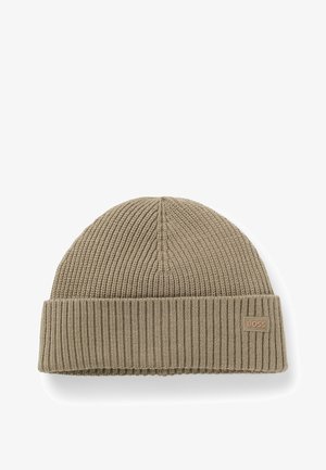 Gorro de punto beige con textura acanalada y un dobladillo. Presenta un pequeño parche de logo de marca en el lado.