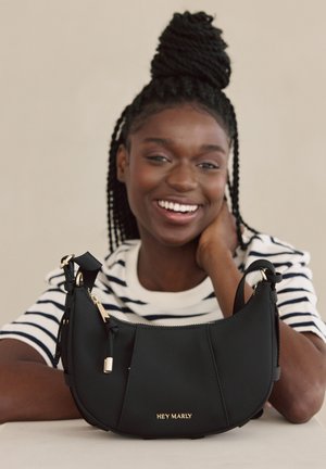 Schwarze Handtasche aus weichem Material mit geschwungener Form, goldenen Hardware-Elementen und einem Reißverschluss. Mit geprägt: "HEY MARLY."