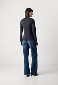 Smal passform mørkegrå langermet genser kombinert med vide blå denimjeans. Jeansene har en klassisk lommeutforming og lett slitasje på sømmene.