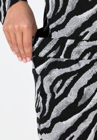 Zwart-witte stof met zebra-patroon, hand reikt naar een zijvak; de textuur lijkt zacht en structuur te hebben met contrasterende strepen.