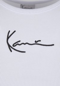 Tissu blanc côtelé avec un col rond mettant en valeur une signature noire brodée de manière proéminente. La texture de la surface est verticale et détaillée.