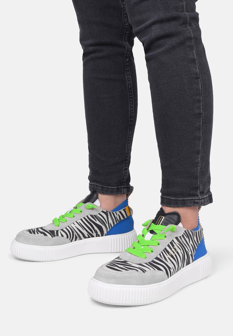 Sneaker con motivo zebra in suede grigio, lacci verdi, accenti blu e una spessa suola bianca. Il design testurizzato contrasta con materiali lisci.