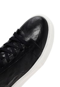 Black leather sneaker with a smooth texture, featuring round toe, lace-up design, and a white rubber sole. Simple and minimal detailing.