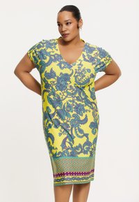 Kurzärmliges gelbes Kleid mit V-Ausschnitt, das mit einem lebhaften aqua-farbenen Blumenmuster und einem bedruckten Saum mit geometrischen Akzenten versehen ist. Glatte Stoffstruktur.