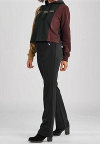 Felpa corta con cappuccio in nero, bordeaux e marrone chiaro con logo dorato; abbinata a pantaloni elasticizzati neri e stivaletti alla caviglia.