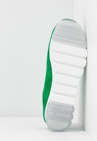 Sneaker verde in suede con suola in gomma bianca, dotata di una presa testurizzata e un tacco arrotondato. La vista laterale mette in evidenza la transizione del materiale regolare.