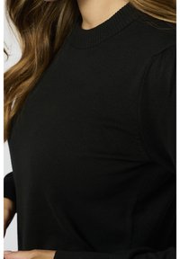Maglione nero lavorato a maglia con scollo rotondo, polsini a coste e una superficie testurizzata, che mette in risalto un design di maniche aderenti e leggermente a sbuffo.