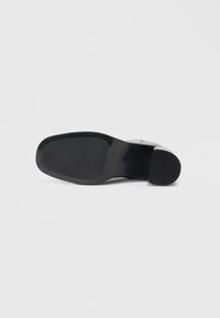 Suola nera di scarpa con una superficie liscia e piatta e bordi arrotondati; design minimale, finitura opaca e senza modelli o accenti visibili.