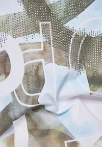 Weißer Stoff mit einem hellblauen und braunen abstrakten Muster, das glänzende silberne Nieten in einem Verlauf über das Design anordnet.