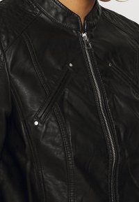 Giacca in pelle nera con colletto rotondo, tasche diagonali con zip e accessori lucidi. Finitura testurizzata con dettagli di cucitura sottili.