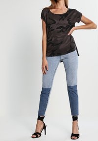 Černý top s maskáčovým vzorem a krátkým rukávem, spárovaný s světle modrými džínami s tmavě modrým a světle modrým patchworkem. Černé sandály na vysokém podpatku.