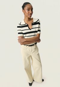 Gebreide top met zwart-witte strepen, V-hals en geschulpte kraag; gecombineerd met crèmekleurige wide-leg broek en zwarte puntige schoenen.