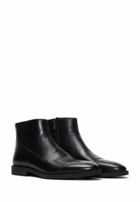 Botas de cuero negro hasta el tobillo con un acabado suave, puntera redondeada, paneles laterales elásticos y cierre con cremallera en el lado exterior. Suela plana.