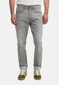 Lys grå jeans med lige pasform, subtil struktur, standard fem-lomme design og opkrøllede ben, parret med olivengrønne sko.