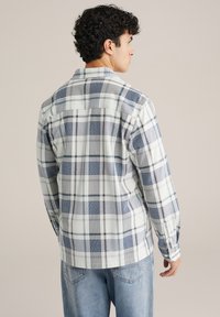 Miesten pitkähihainen paita valkoisella ja tummansinisellä ruutukuvioinnilla, jossa on napillinen kaulus ja istuvat kalvosimet, valmistettu kudotusta kankaasta.