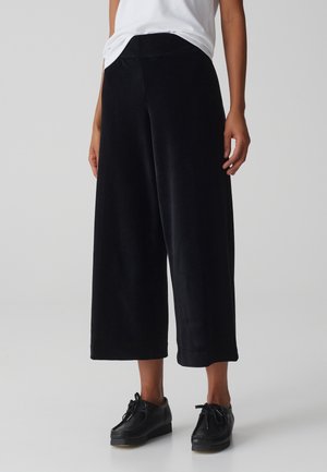 Černé manšestrové culottes s širokými nohavicemi, strukturovanou látkou, vysokým pasem a bočními kapsami, doplněné černými šněrovacími botami.