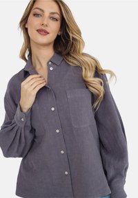 Szara, długosleeve koszula zapinana na guziki w teksturowanej tkaninie. Posiada jedną kieszeń z przodu oraz zaokrąglony kołnierzyk. Guziki są w jasnym kolorze.