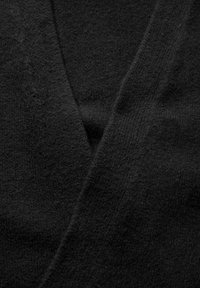 Svart cardigan tyg med en mjuk, texturerad yta; har en v-ringad design och överlappande paneler. Inga synliga mönster eller detaljer.
