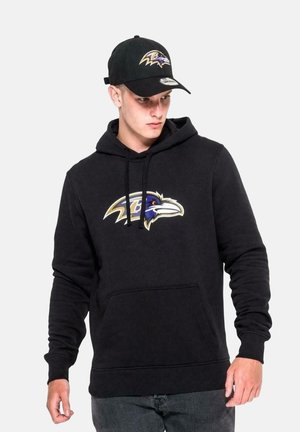 Black hoodie with a front pocket and loose fit, featuring a Ravens logo in purple and gold on the chest. Paired with a matching black cap.