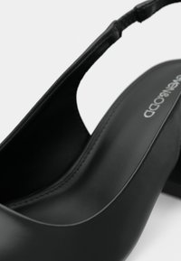 Chaussure noire à talon ouvert avec une finition en cuir lisse, bout rond et design minimaliste. Présente des coutures visibles et un petit talon.