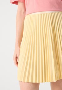 Gonna gialla a pieghe realizzata in tessuto leggero con superficie testurizzata. Vita elastica per il massimo comfort. Design semplice e pulito.