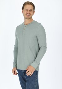 Vaaleanvihreä pitkähihaisen henley-paita, jossa on kolme puupainiketta, ribbitetty pinta ja rento malli, yhdistettynä sinisiin farkkuihin.