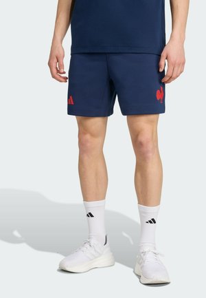 Navy blue athletic shorts with red Adidas logo and rooster emblem. Worn with white socks featuring black stripes and white sneakers.