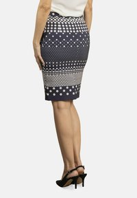 Falda lápiz navy con un patrón de lunares en degradado en color crema, diseño ajustado, de longitud media, acompañada de unos zapatos de tacón alto negros.