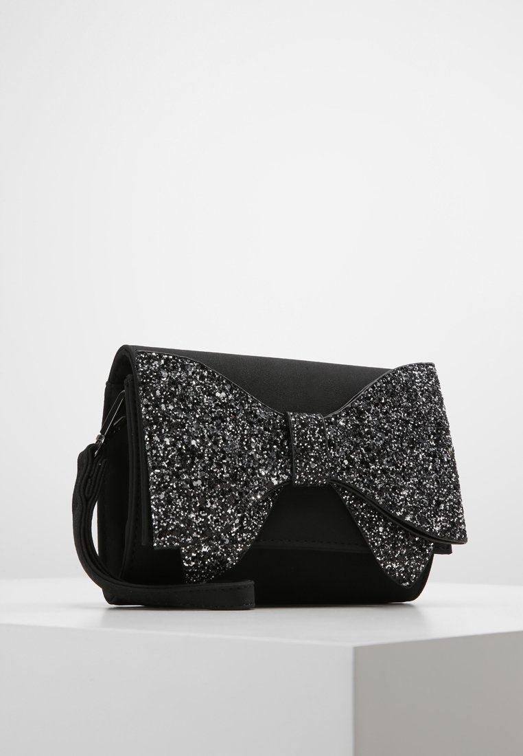 Sac à main synthétique noir avec un grand nœud noir étincelant. Dispose d'une fermeture éclair et d'une sangle amovible. Texture lisse avec des accents pailletés.