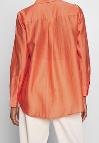 Camicia a manica lunga in un vivace corallo, con una superficie satinata liscia, colletto classico, polsini con bottone e orlo curvo.