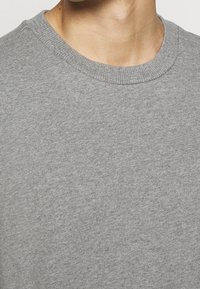 Sudadera gris con cuello redondo y tejido texturizado, con un acabado suave y sin patrones ni detalles visibles.