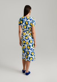 Blumenkleid mit kurzen Ärmeln; zeigt einen blauen und gelben Zitronendruck auf weißem Hintergrund. Gerade Silhouette und knielanger Saum.
