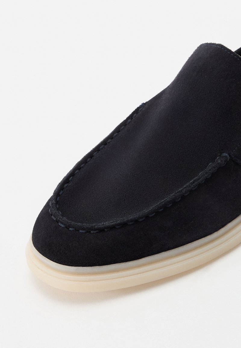 Granatowe zamszowe buty wsuwane z przeszyciami i kremową gumową podeszwą. Posiadają okrągły czubek i gładką fakturę.