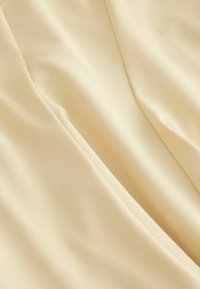 Tejido liso de color beige claro con pliegues sutiles y detalles de costura, que muestra una textura suave y ligeramente brillante.