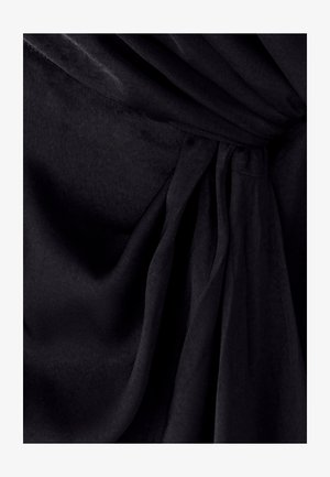 Tela negra con una textura suave, que presenta pliegues drapeados y un detalle anudado en la cintura; la superficie parece blanda y ligeramente lustrosa.