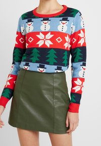 Stickad tröja med snögubbe- och trämönster i blått, rött och grönt, tillsammans med en mörkgrön läder minikjol.
