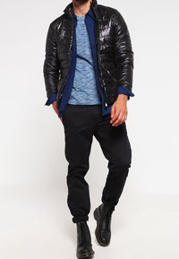 Black padded jacket, blue patterned shirt, black pants, and black boots. The jacket has a shiny texture and a zipper front.